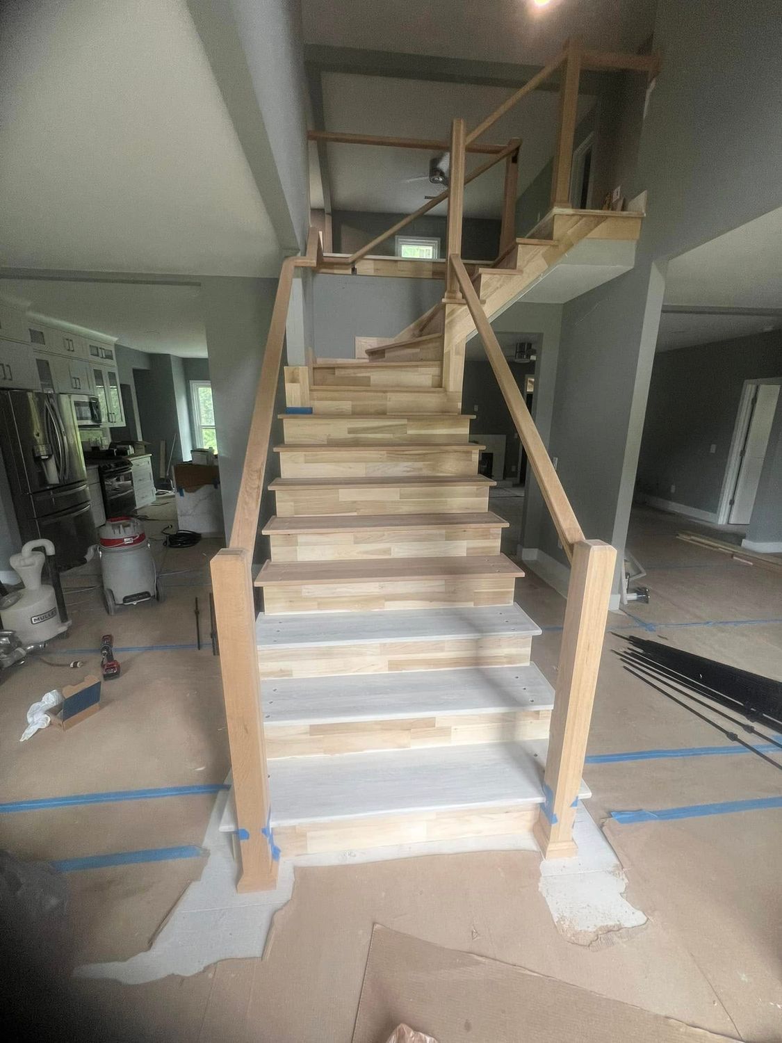 Wooden staircase under construction with railing and newel posts. Interior setting.