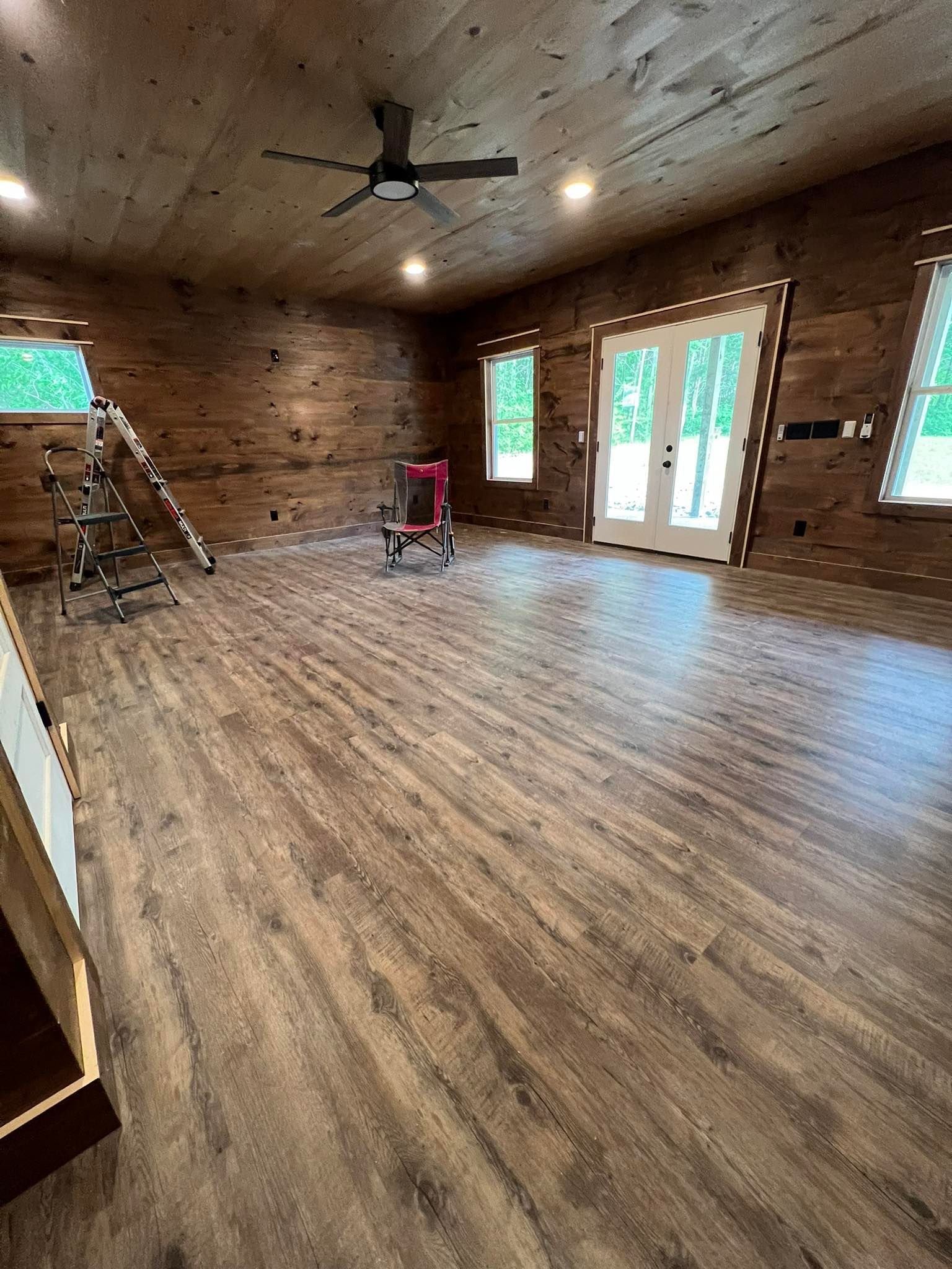 Empty room with wood paneling on the walls and ceiling, wood-look flooring, windows, and French doors.