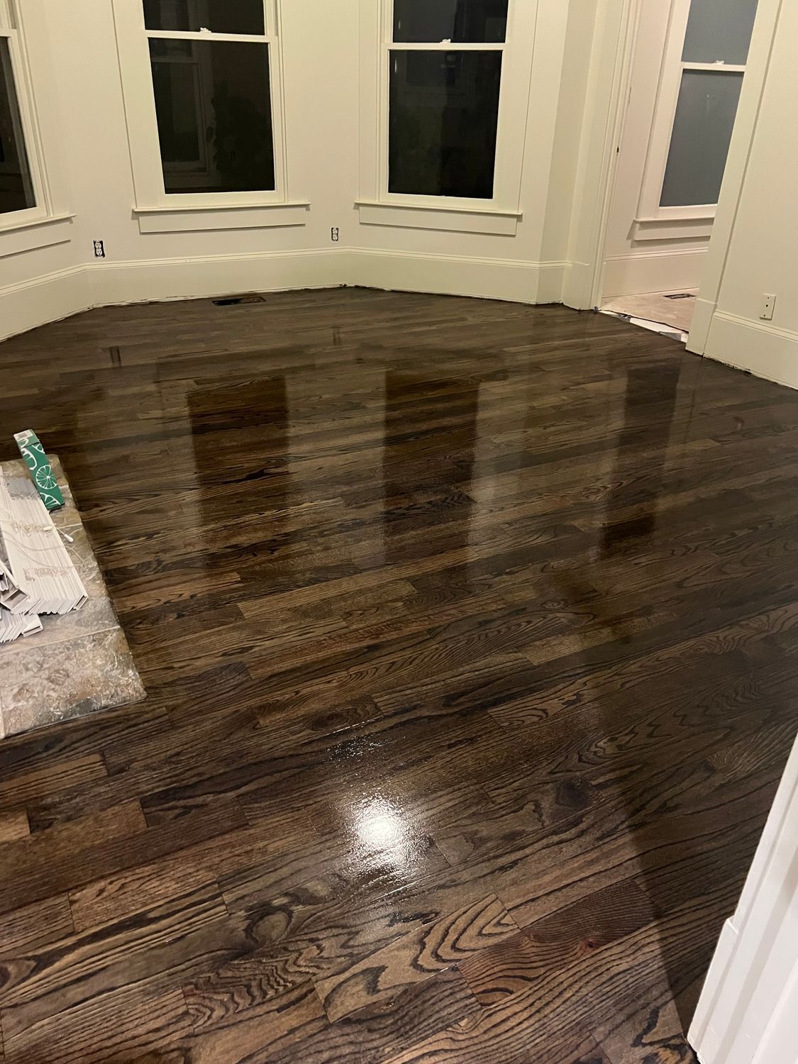 Shiny, dark-stained hardwood floor reflecting light in a room with white trim and windows.