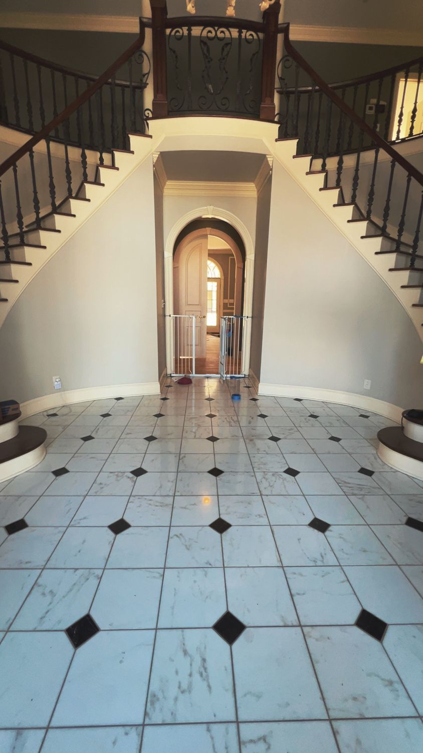 Grand foyer with marble tile floor and dual staircases. A person is seen walking towards a doorway.