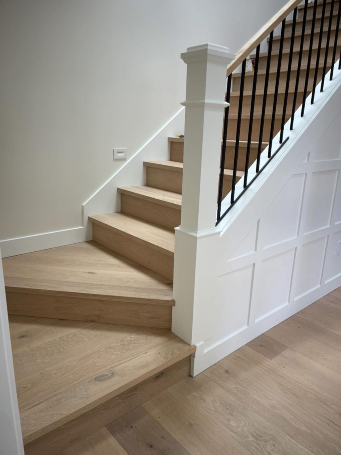 Wooden staircase with white trim, black railings, and panelled wall.