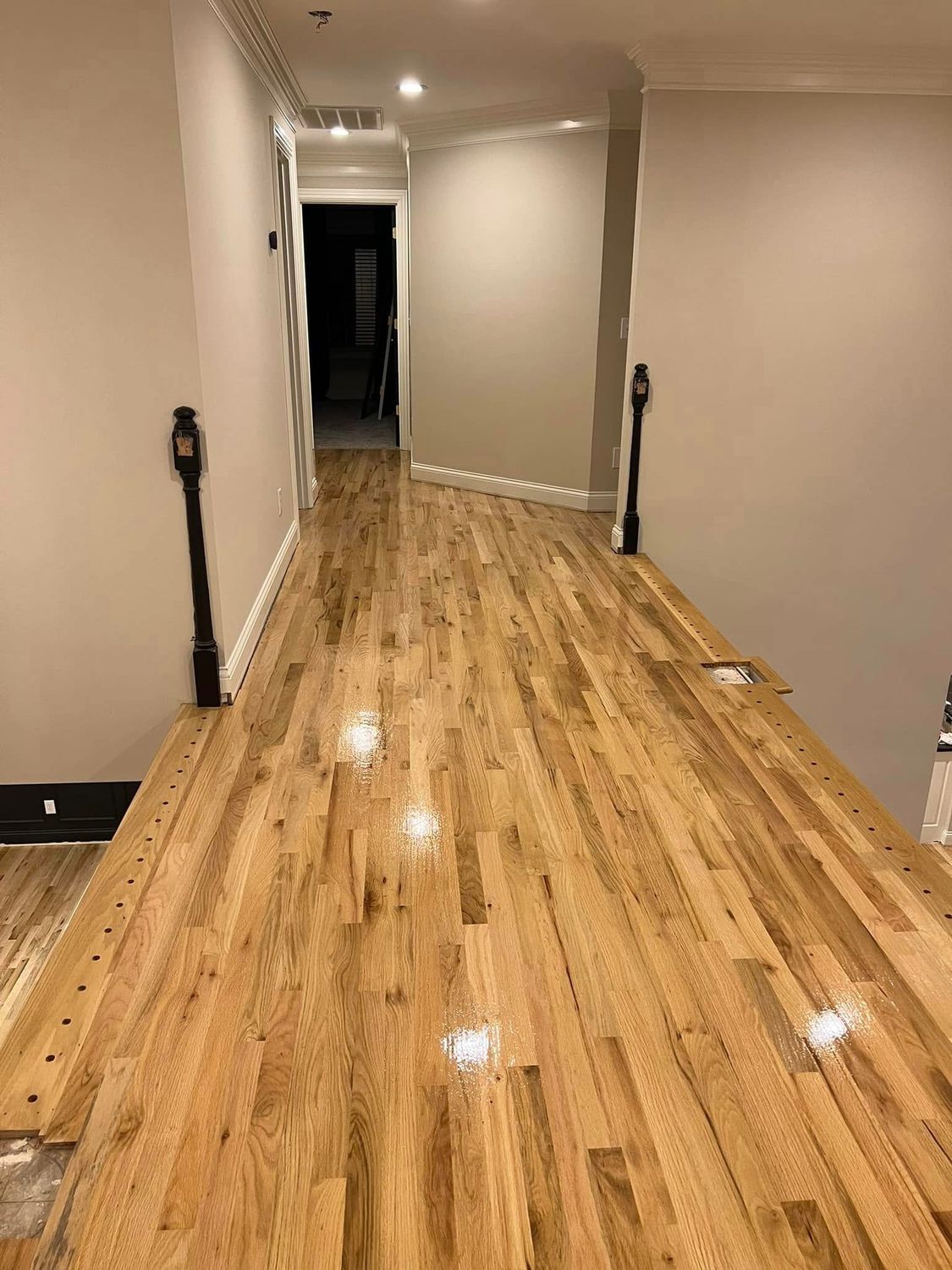 Hallway with newly installed wooden floor, beige walls, and dark banisters.