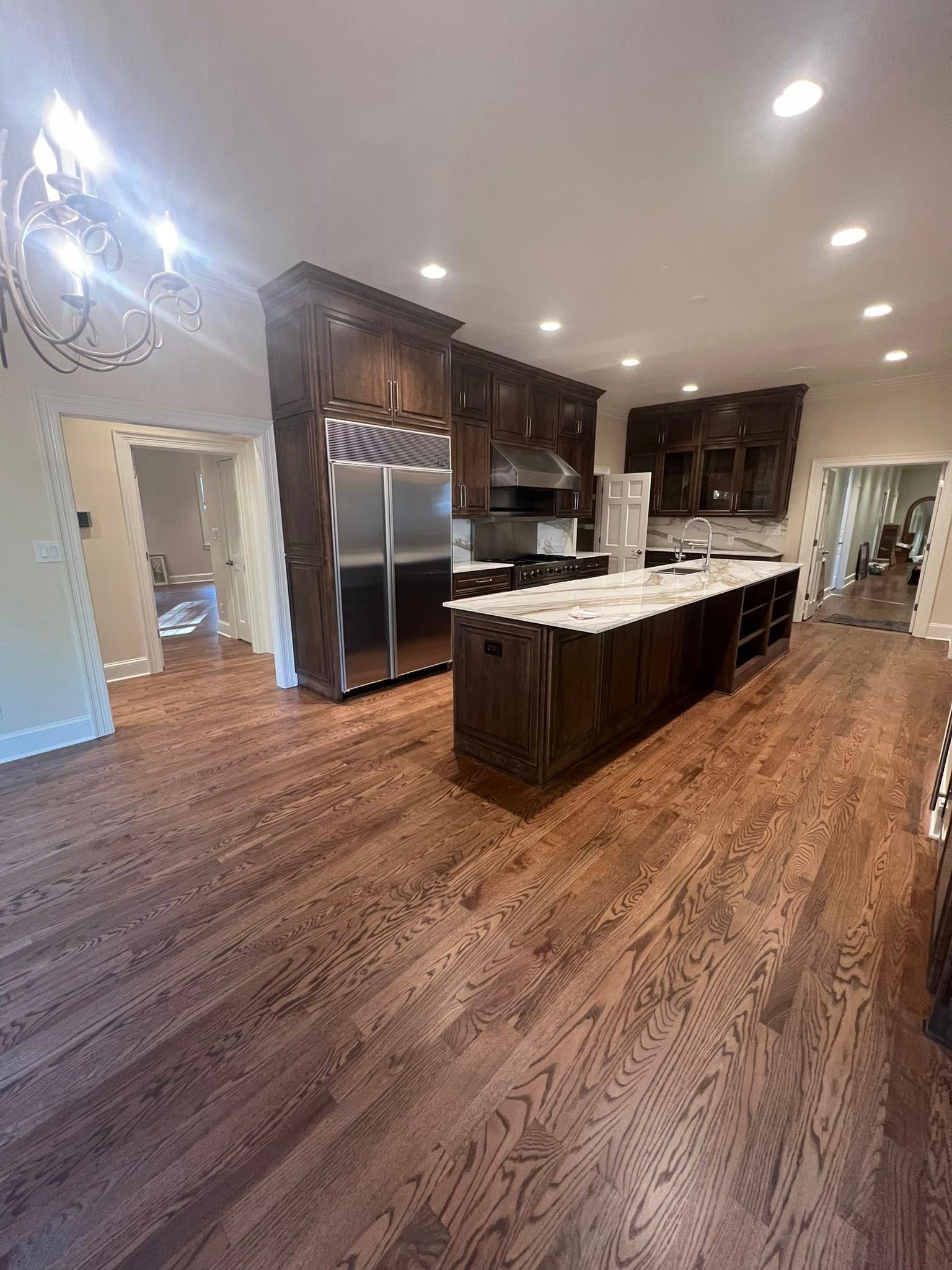 Dark wood kitchen with island, stainless steel refrigerator, and recessed lighting.
