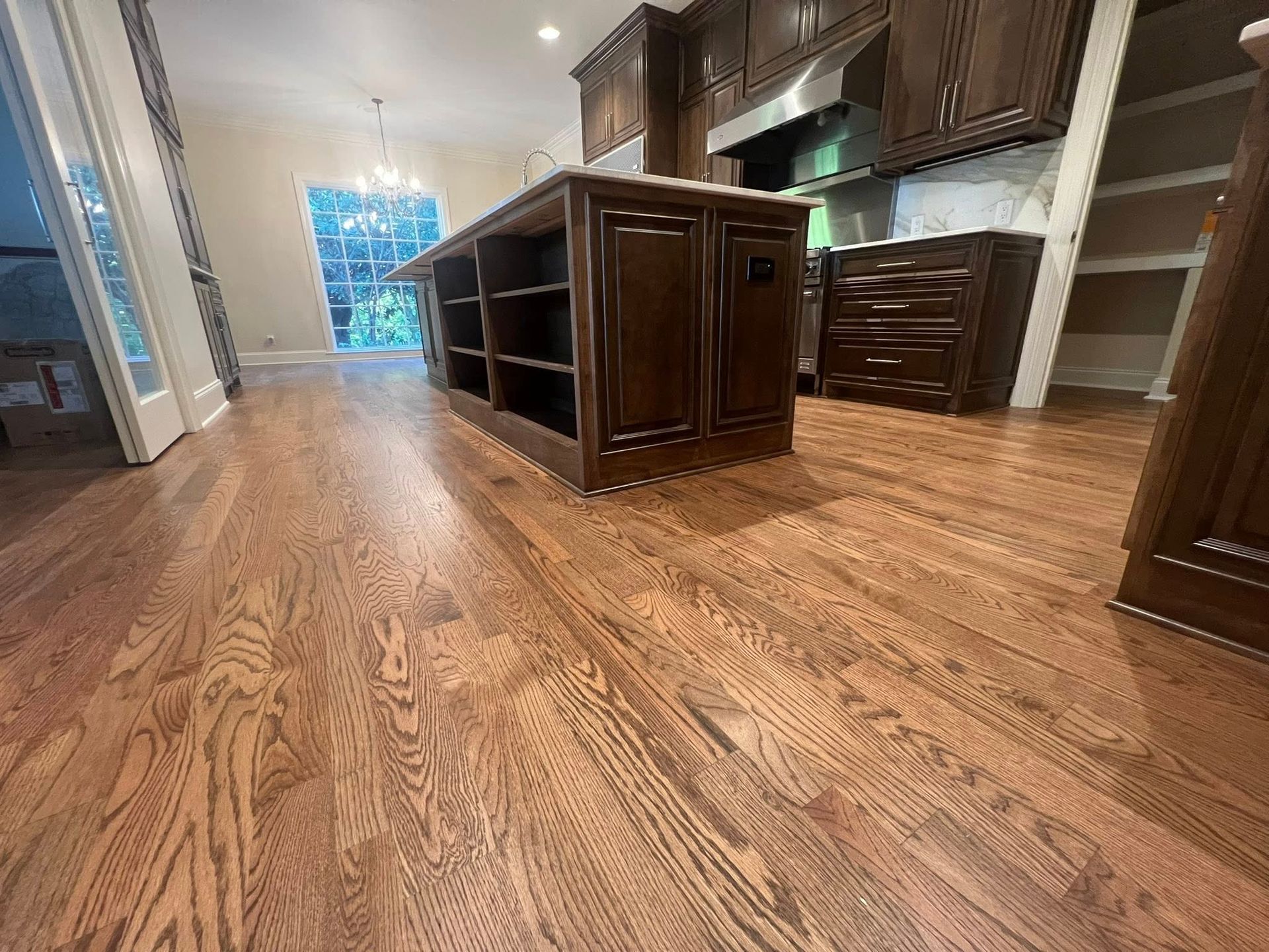 Hardwood floors in a kitchen with a dark wood island and cabinets. Bright light comes from a window.