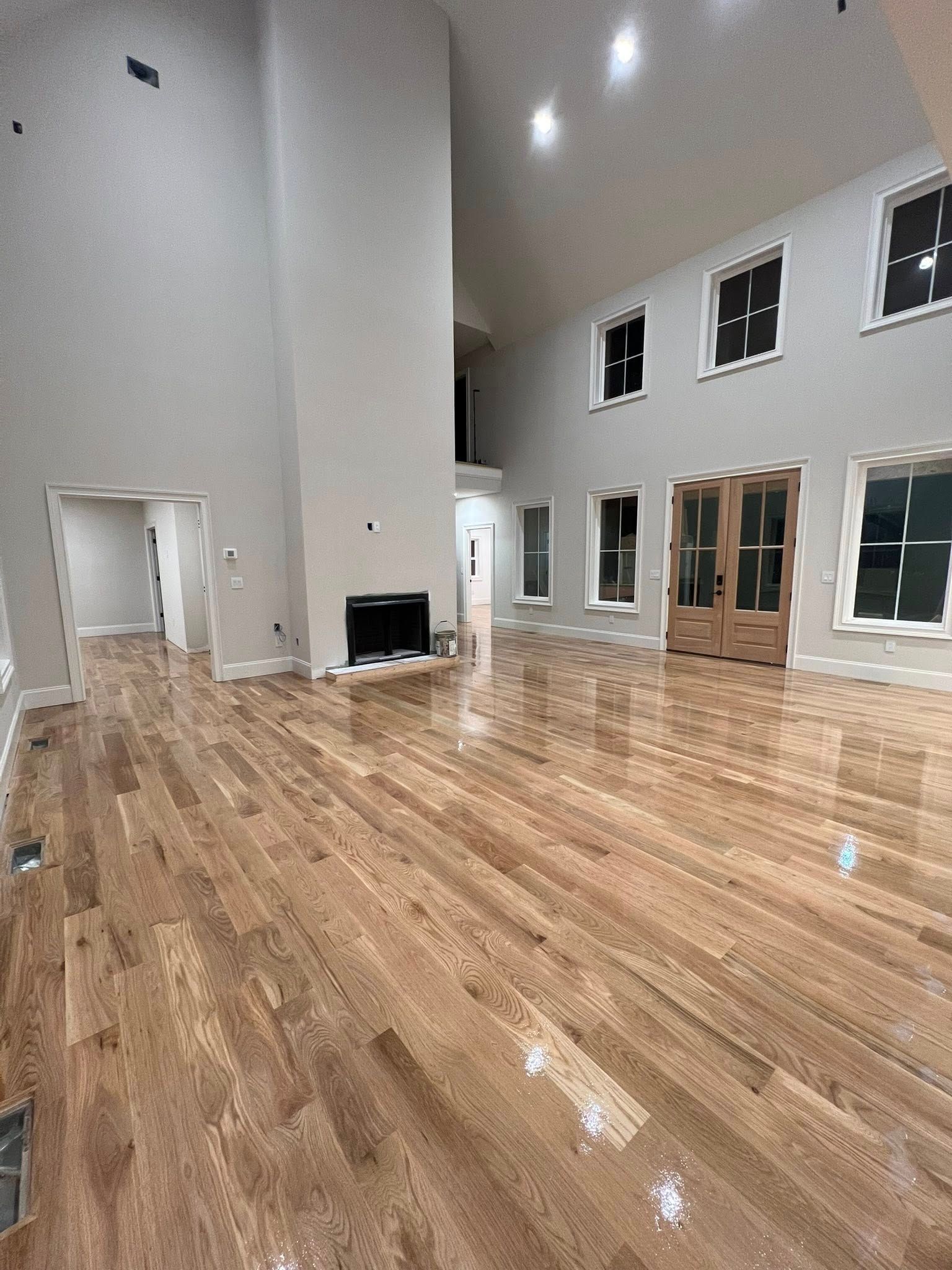 Spacious living room with hardwood floors, tall ceilings, fireplace, and large windows.