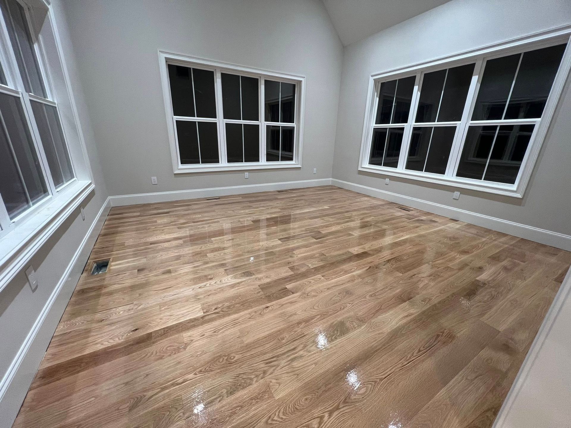 Empty room with hardwood floors, light gray walls, and multiple windows with white trim.