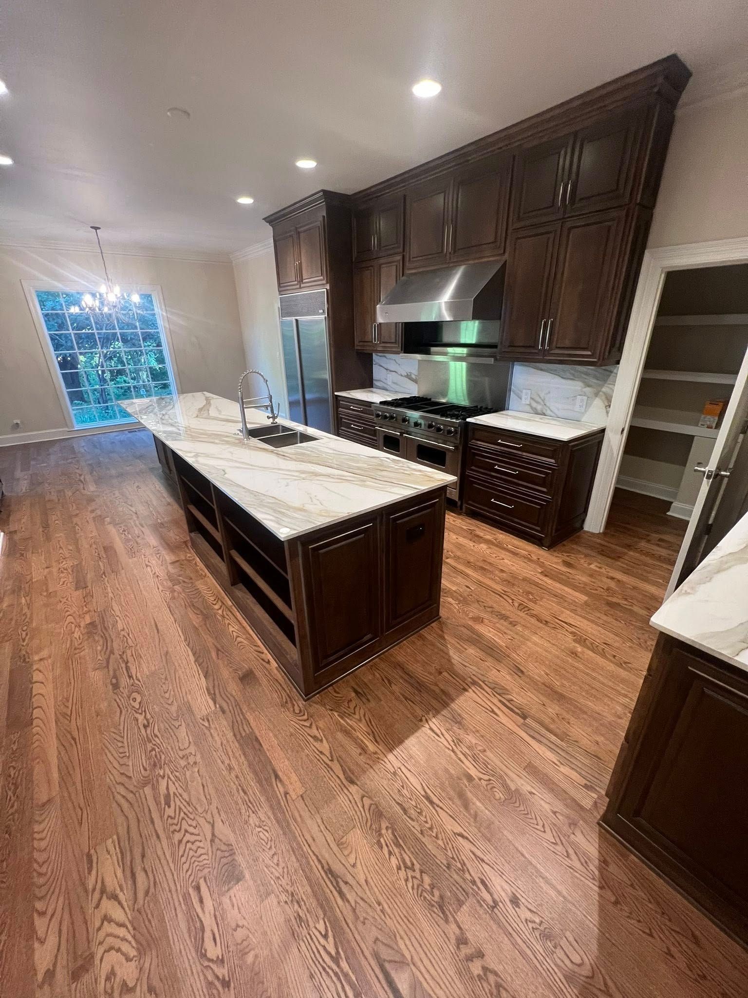 Dark wood kitchen with a large island, stainless steel appliances, and white countertops.