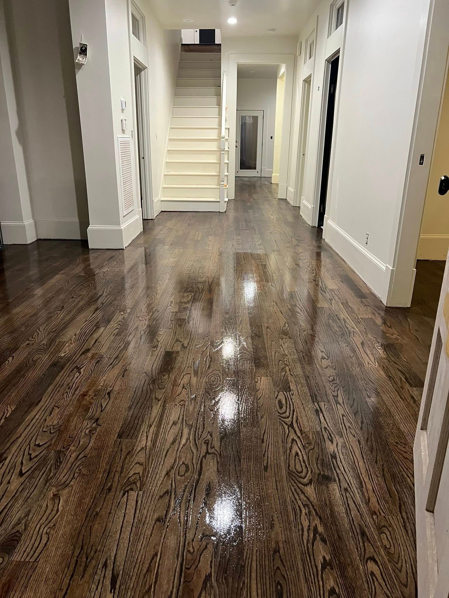 Long hallway with glossy, dark wood floors reflecting the light; stairs lead upward at the end.