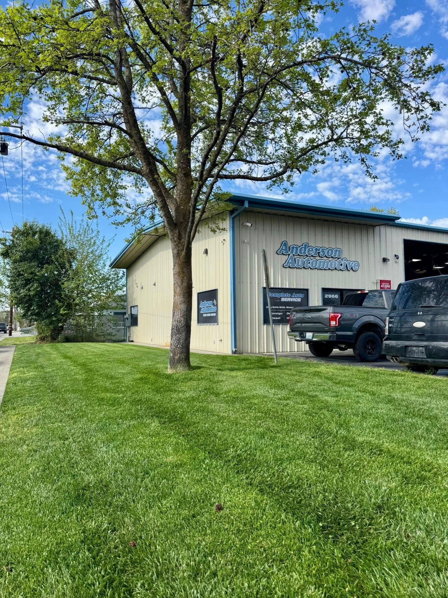 Auto repair shop with green grass lawn and a tree. A pickup truck is parked outside. Blue sky.