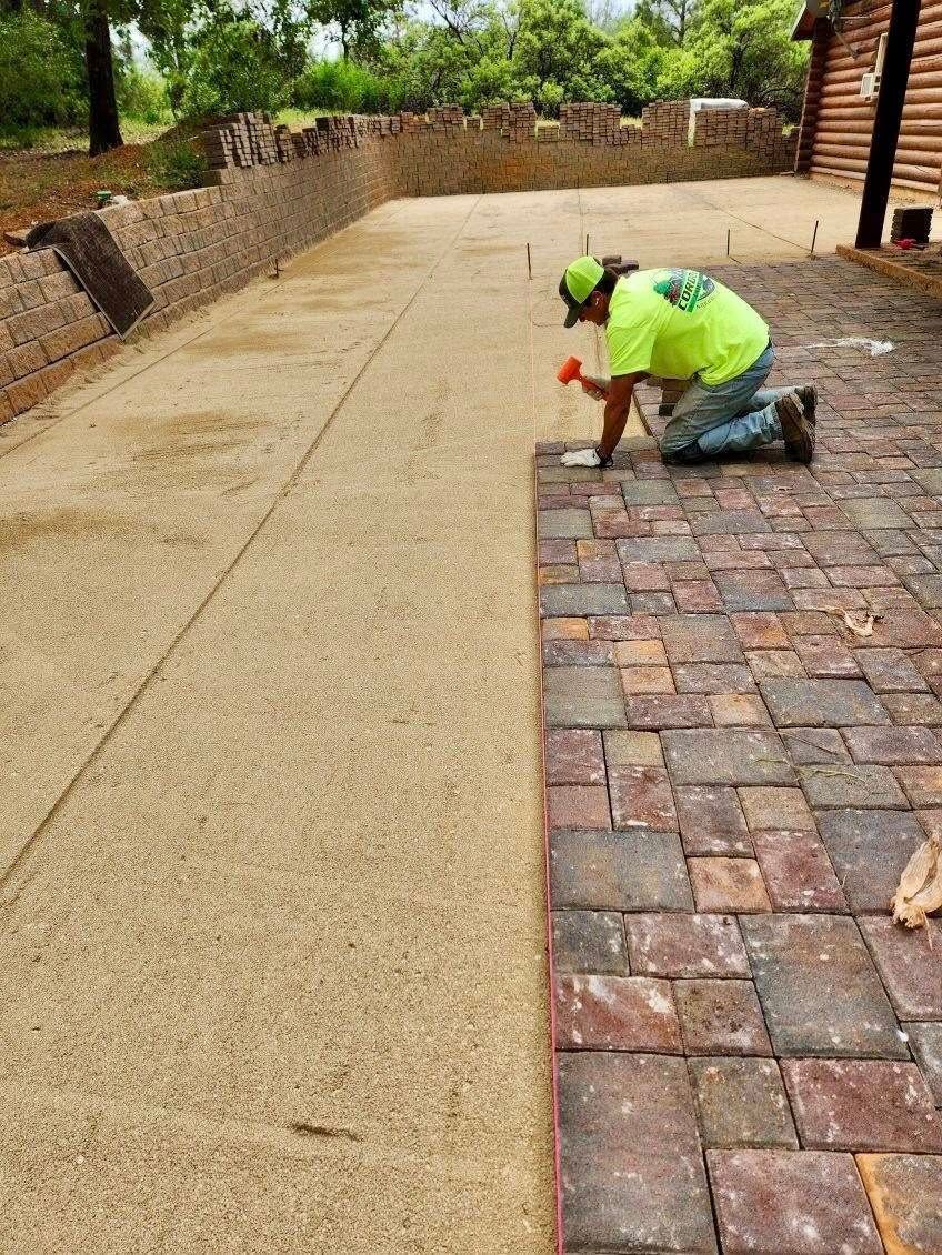 Person laying brick pavers on a walkway, with a section of the path prepared with gravel.