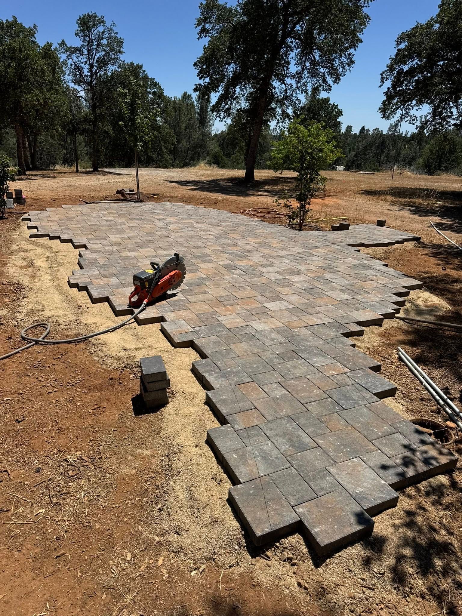 Laying brick pavers for a patio in an outdoor setting. A saw is on the existing pavers.