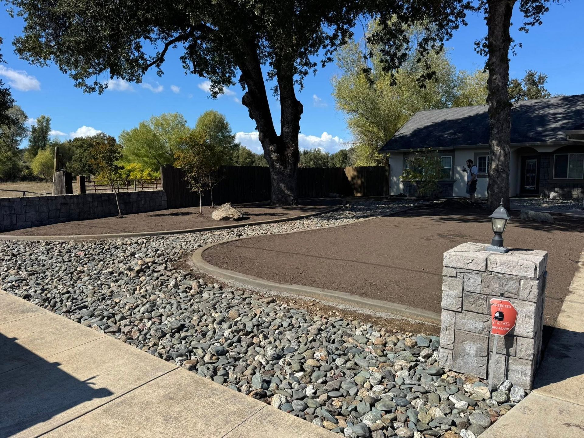 A house with a newly landscaped yard. Gravel walkway, rock border, and fresh mulch with trees and a blue sky.