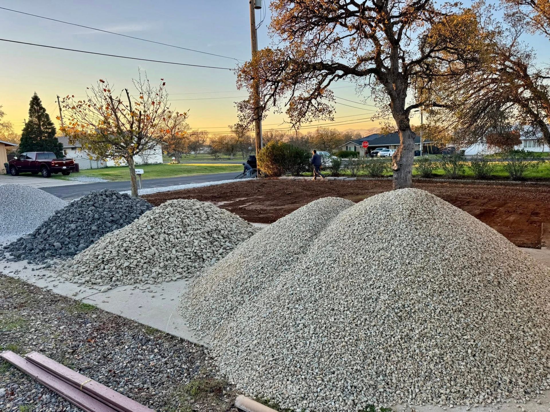 Piles of gravel in various shades, roadside with trees and a car in the distance.