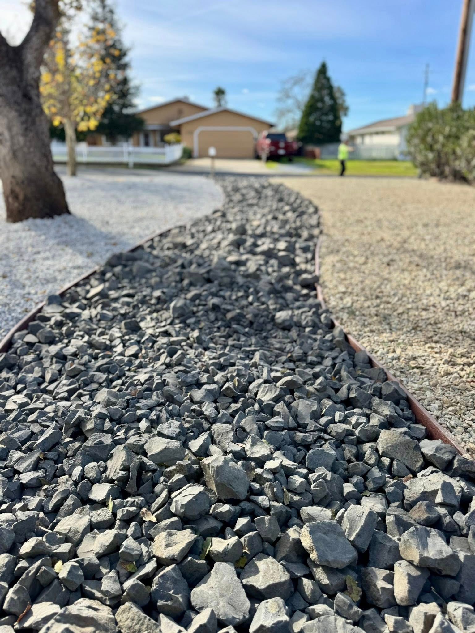 Gravel pathway bordered by metal edging, leading to a house in a residential setting.