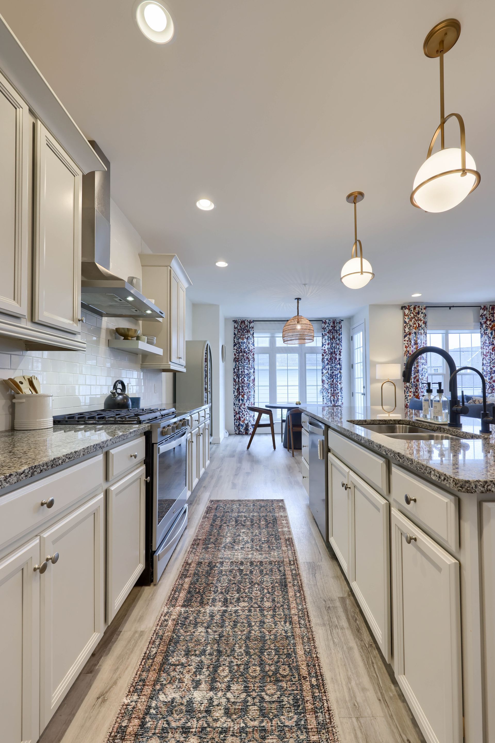 A kitchen with white cabinets , granite counter tops , stainless steel appliances and a rug.