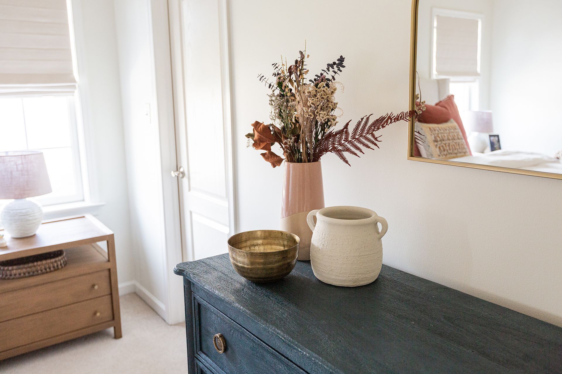 A vase of flowers is sitting on a dresser in a bedroom next to a mirror.