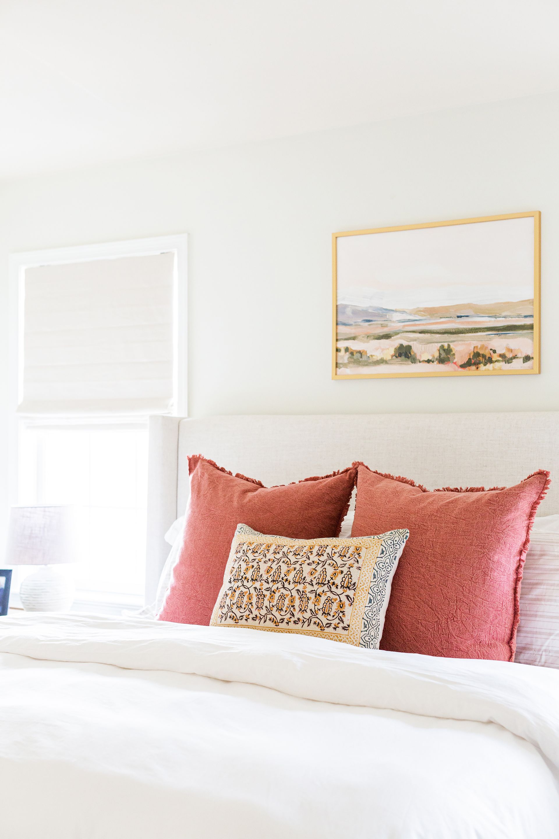A bedroom with a bed , pillows , a picture on the wall and a window.