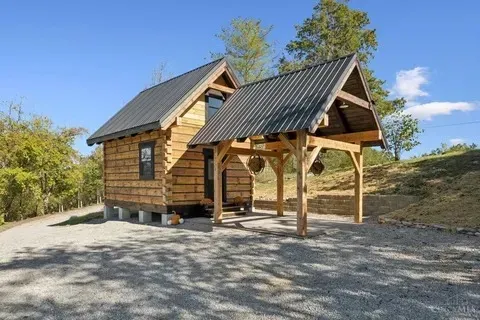 Small wood cabin with covered porch, gravel driveway, and a blue sky.