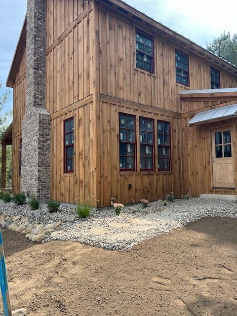 Two-story wood-sided house with brick chimney, windows, and light landscaping.