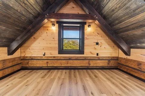 Interior of a wood-paneled attic room with a window, wood beams, and light-colored flooring.