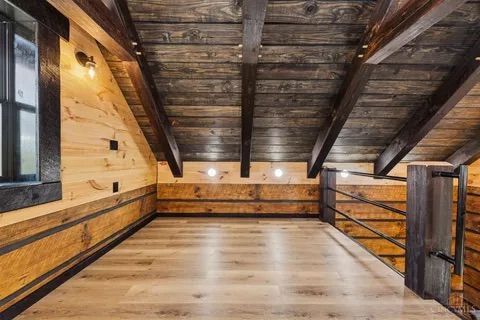Loft area with wood ceiling and light-colored floor, wood-paneled walls, and a black window frame.
