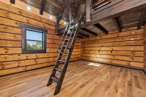 Wooden cabin interior with loft, ladder, and window.