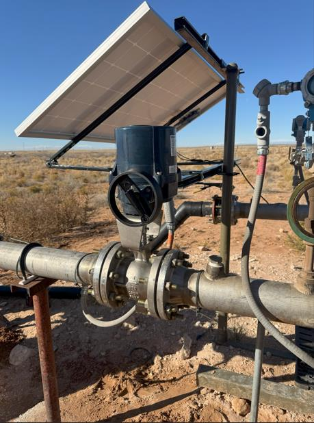 Solar-powered automated valve installed on a metal pipeline in a desert landscape under a clear blue sky.