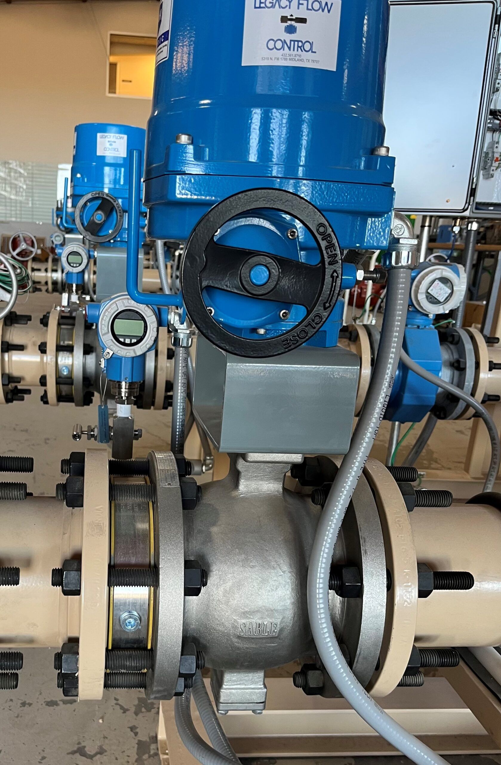 A blue industrial valve actuator mounted on a flanged metal pipe section with a black manual override handwheel.
