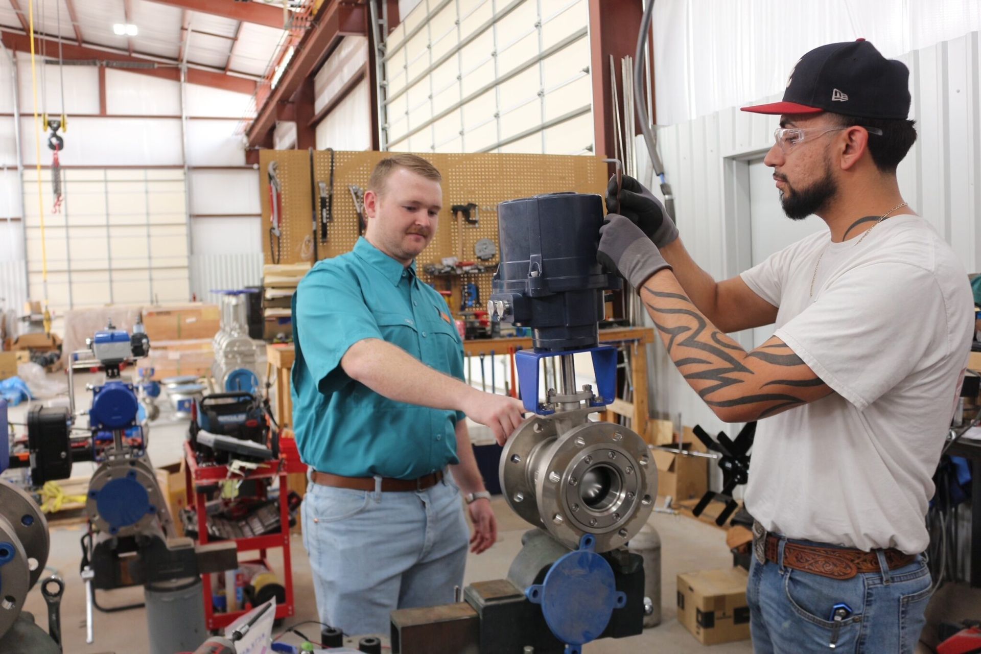 Two technicians in a workshop inspect and assemble a large industrial metal valve.