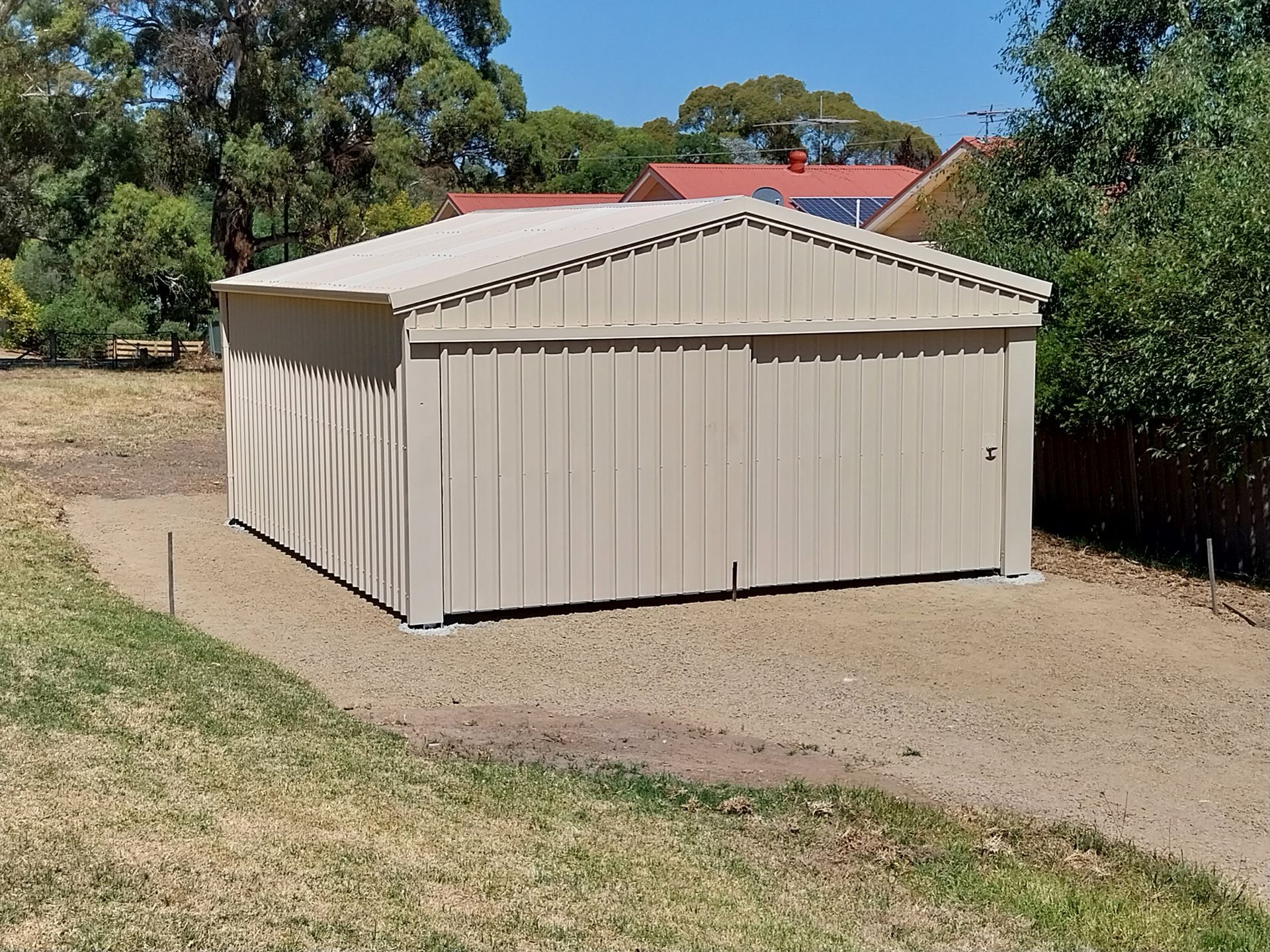 White garden shed surrounded by lush greenery, flowerbeds, and a path.