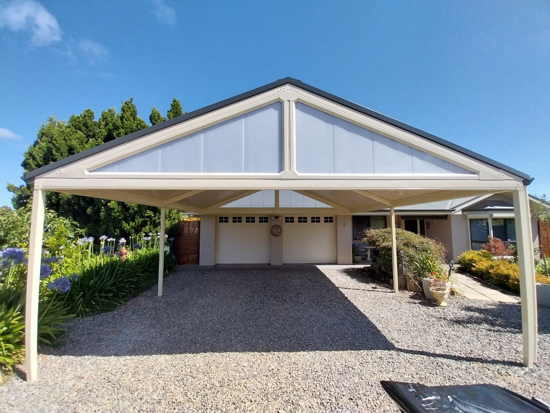 Modern two-story house with a carport. Gray and white exterior, concrete driveway, green lawn.