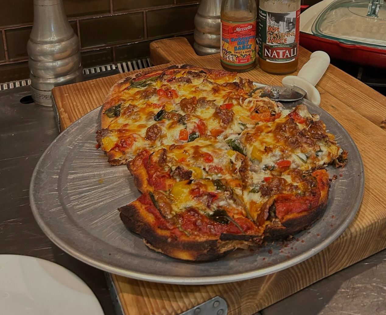 A pizza is sitting on a metal pan on a wooden cutting board