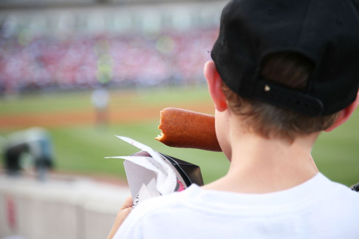 A young boy is eating a corn dog at a baseball game.