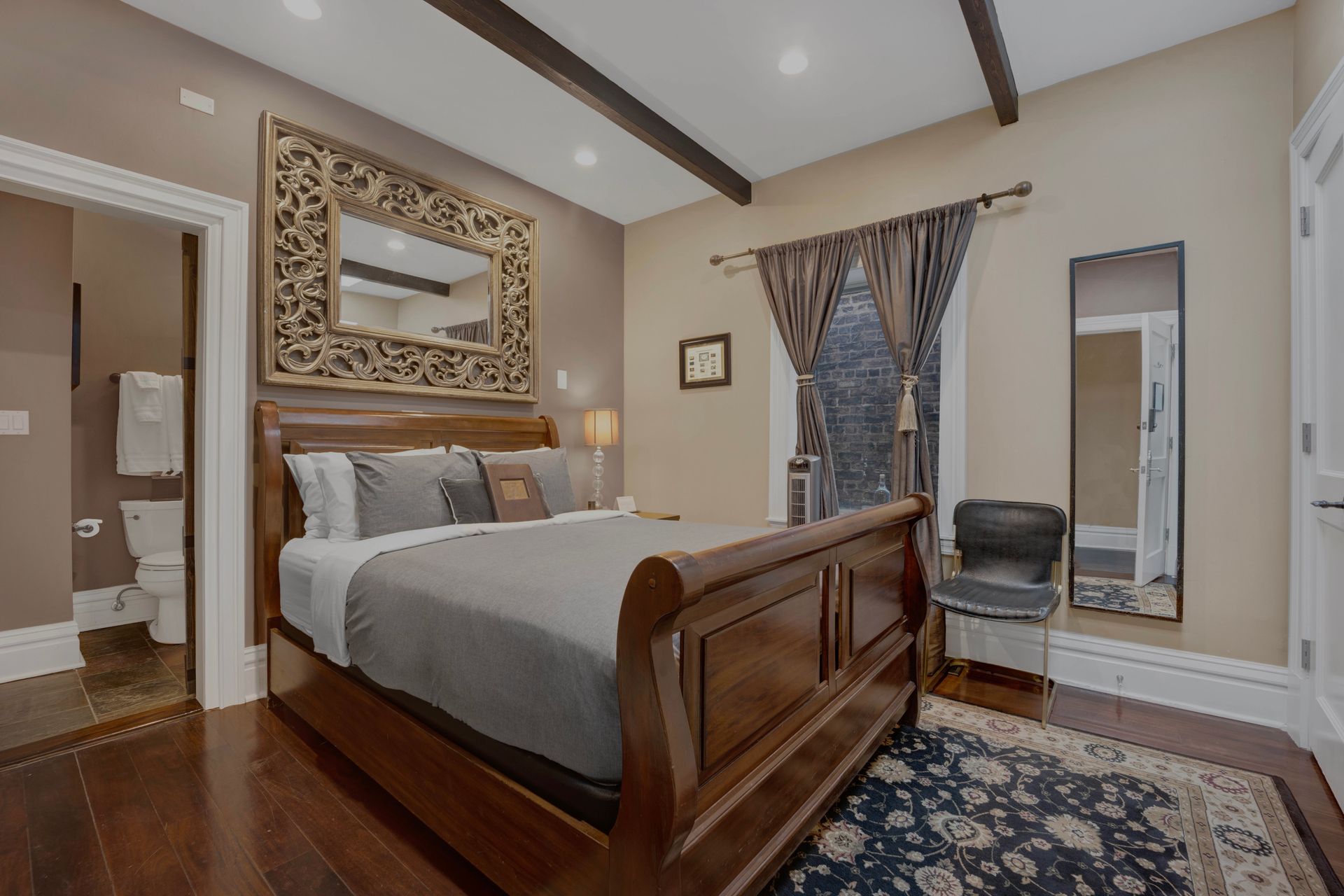 A bedroom with a king size bed , a chair , a mirror and a rug.