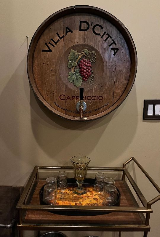 A wooden barrel is hanging on a wall above a bar cart.