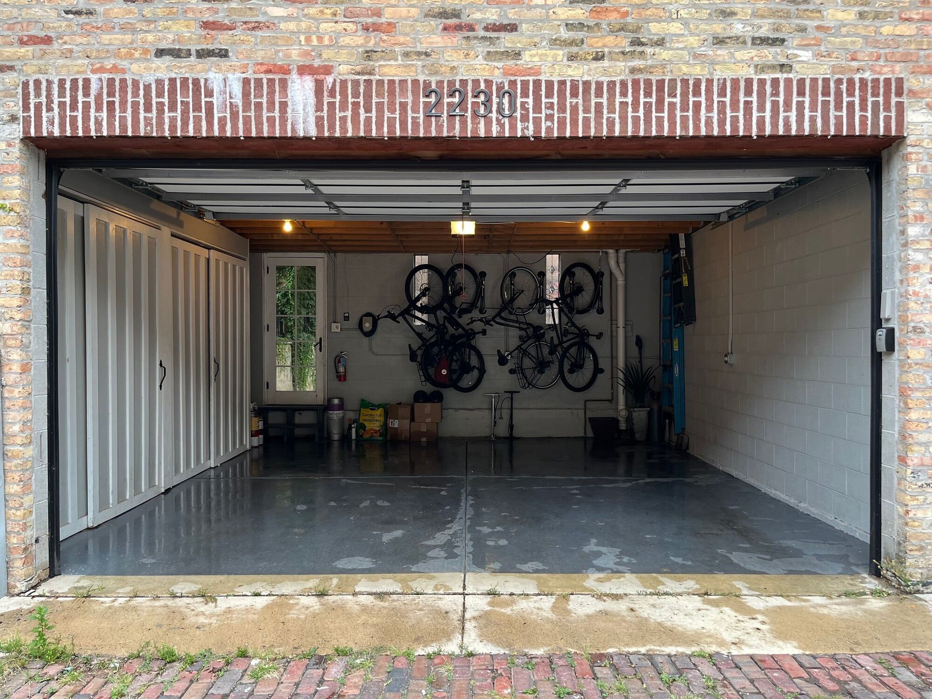 A garage with bikes hanging from the ceiling and a brick wall.
