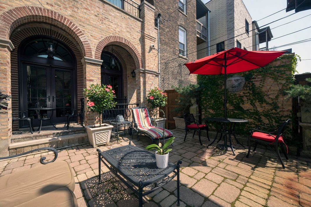 A patio with a red umbrella and chairs in front of a brick building.