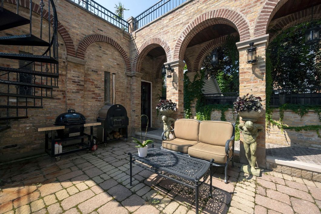 A brick courtyard with a couch , table , and grill.