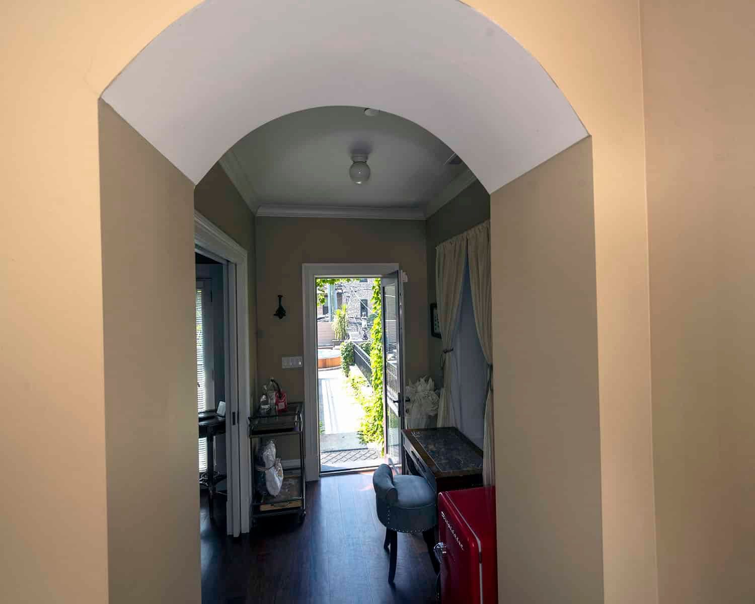 A hallway with an archway leading to a door and a red refrigerator.