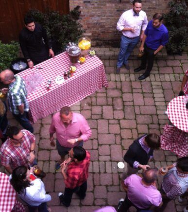 A group of people are gathered around a table with a red and white checkered table cloth