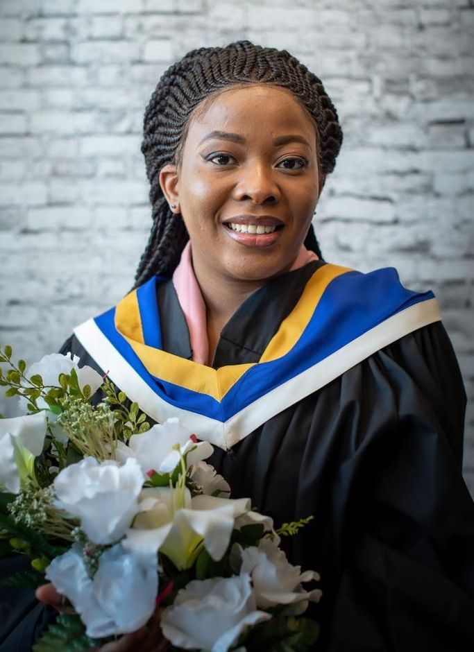 Une femme en robe de remise de diplôme tient un bouquet de fleurs.