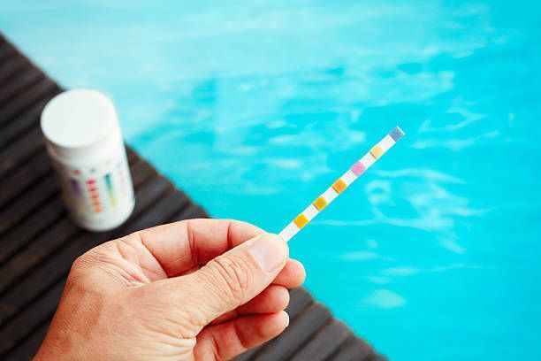 Hand holding a urine test strip over a pool, with a test bottle nearby