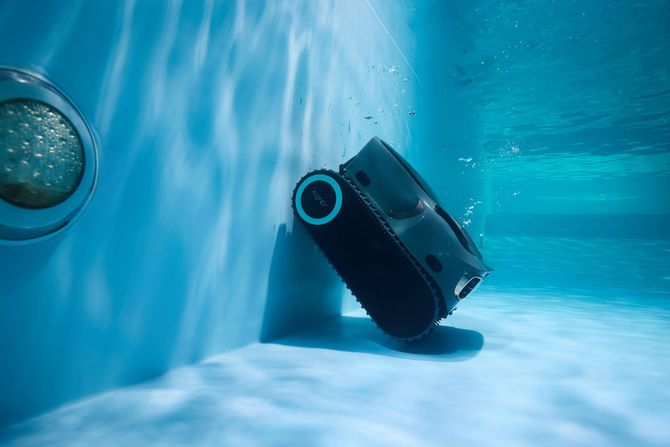 Black pool cleaner floating underwater in a blue swimming pool, tilted against the wall