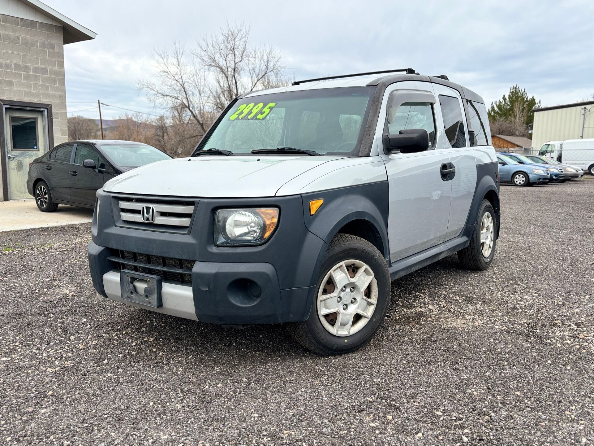 Silver Honda Element SUV parked on a lot, with bright green sale numbers on the windshield.