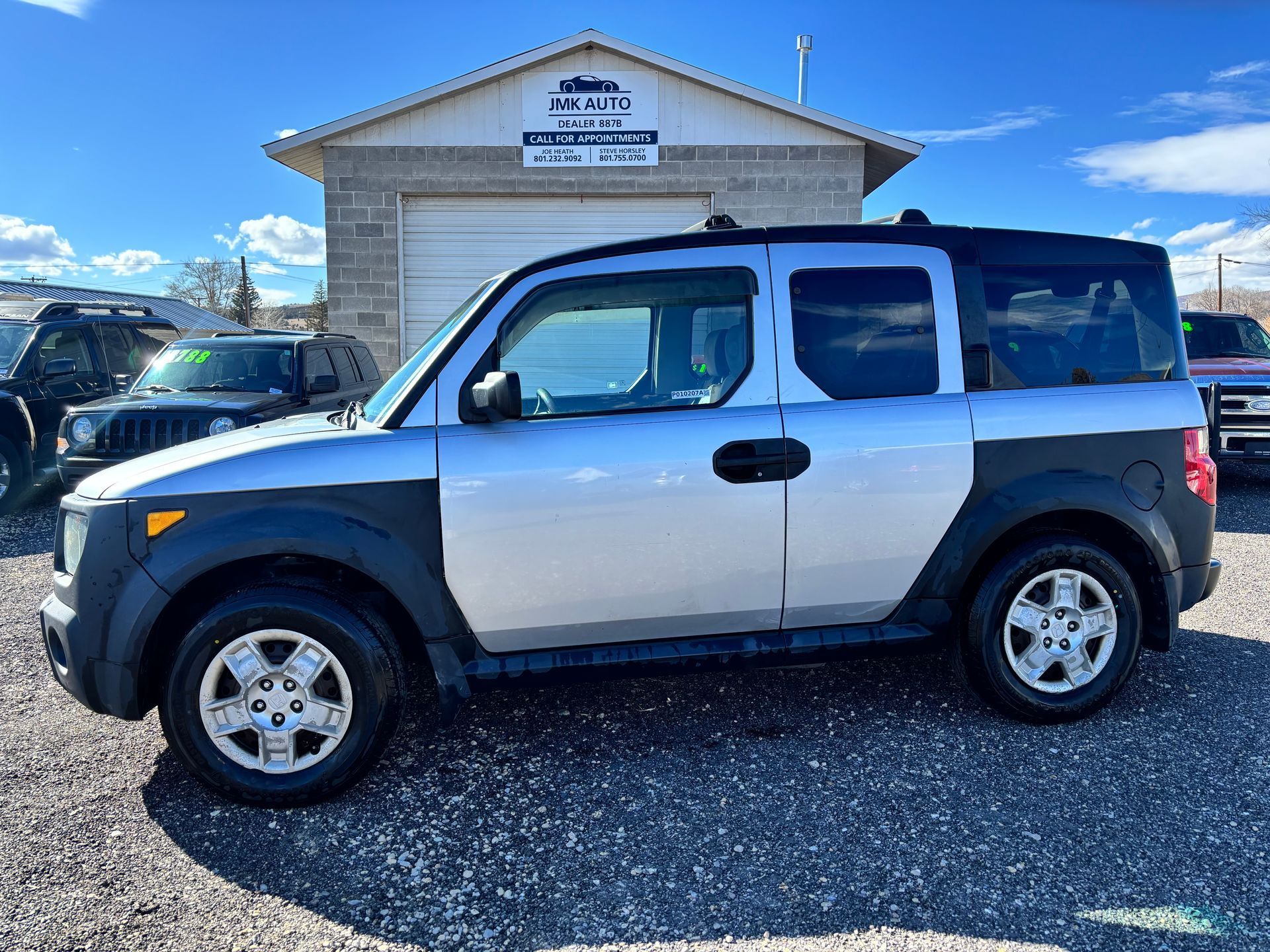 Two-tone white and black SUV parked in front of a small building on a gravel lot