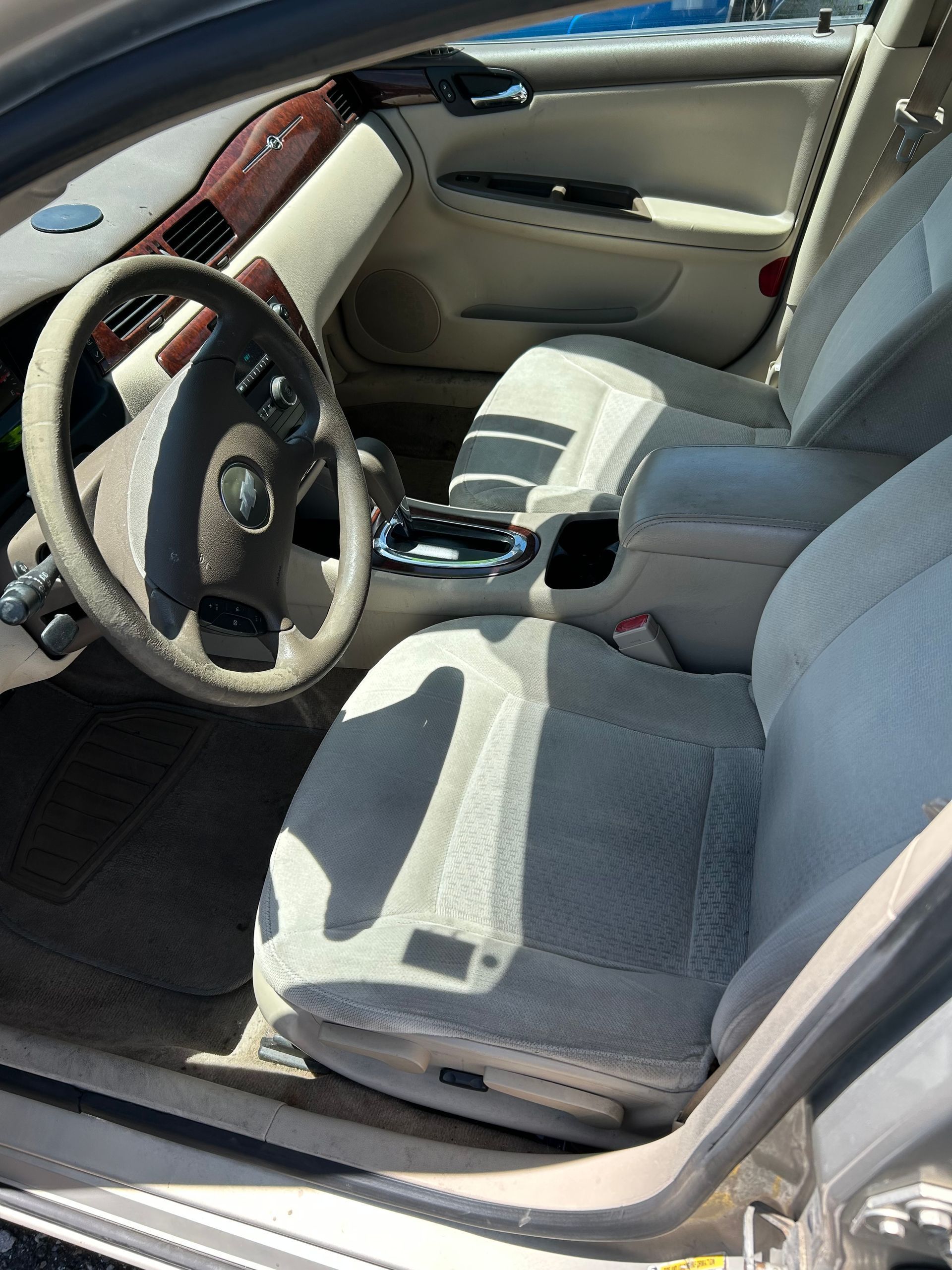 Car interior with beige seats, steering wheel, and center console, viewed from the open door