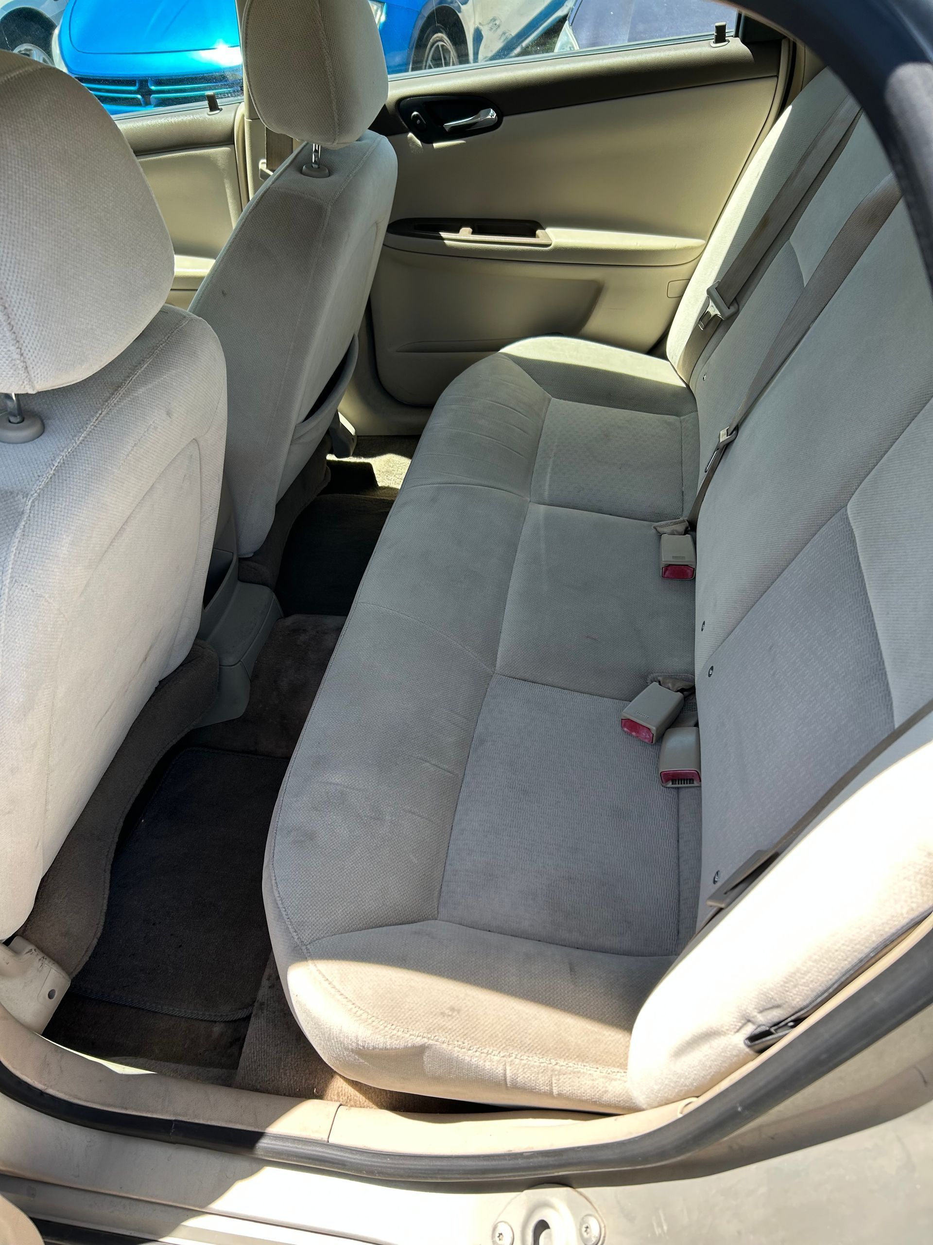Rear car seat with light gray fabric upholstery and black floor mats, viewed from the open door