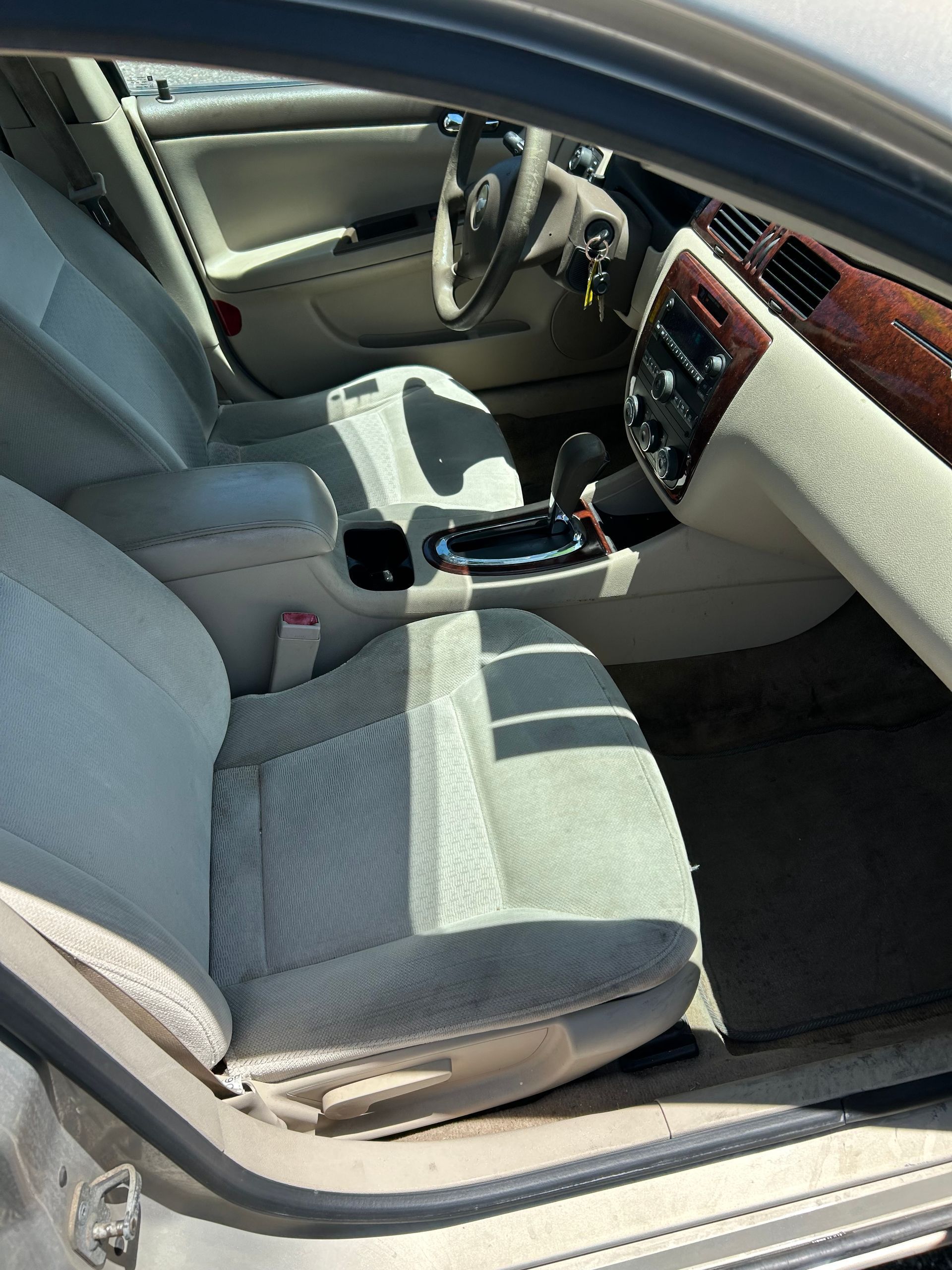 Car interior with gray seats, center console, and wood-trim dashboard viewed from the open door