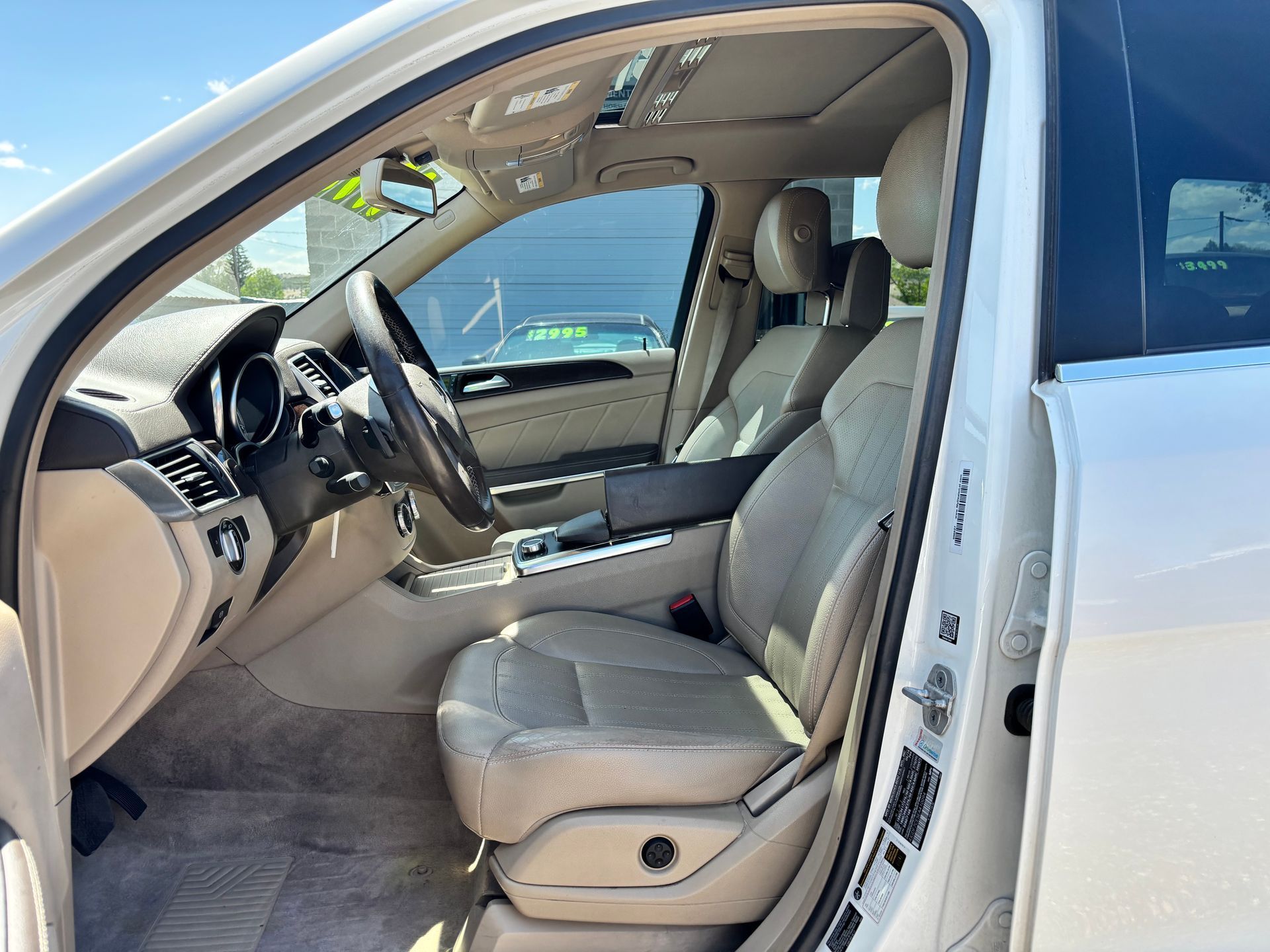 Car interior with driver door open, showing beige front seats and steering wheel.