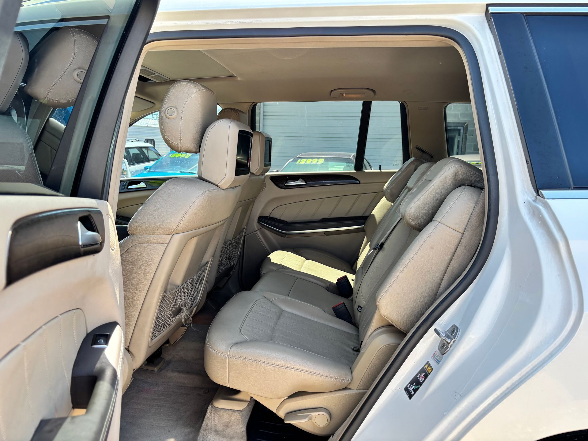 Open rear door showing beige car interior with folded center armrest and headrests